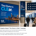 Large digital campaign display inside Cleveland Hopkins Airport terminal with travelers walking through the concourse.